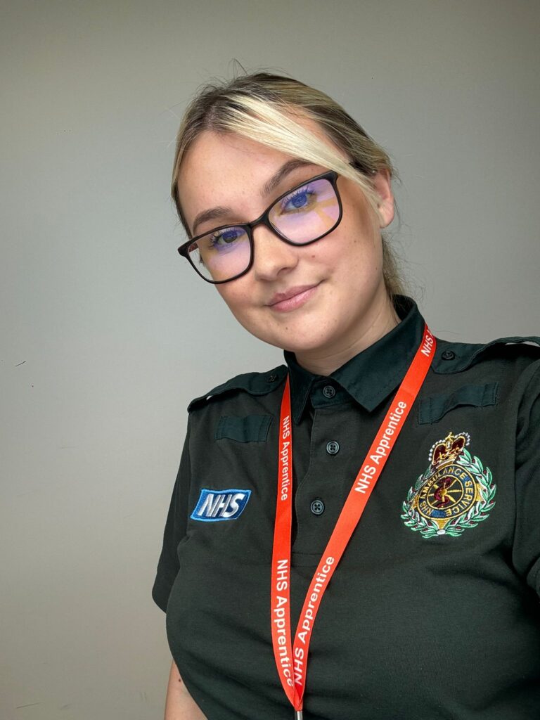A woman, Chloe in Green Paramedic uniform smiling at the camera